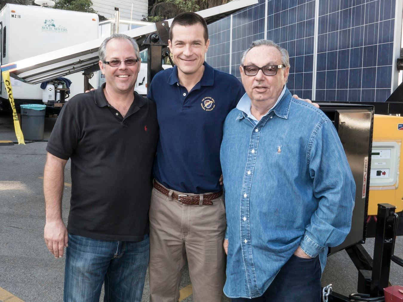 Jason Bateman in front of mobile solar trailer. 